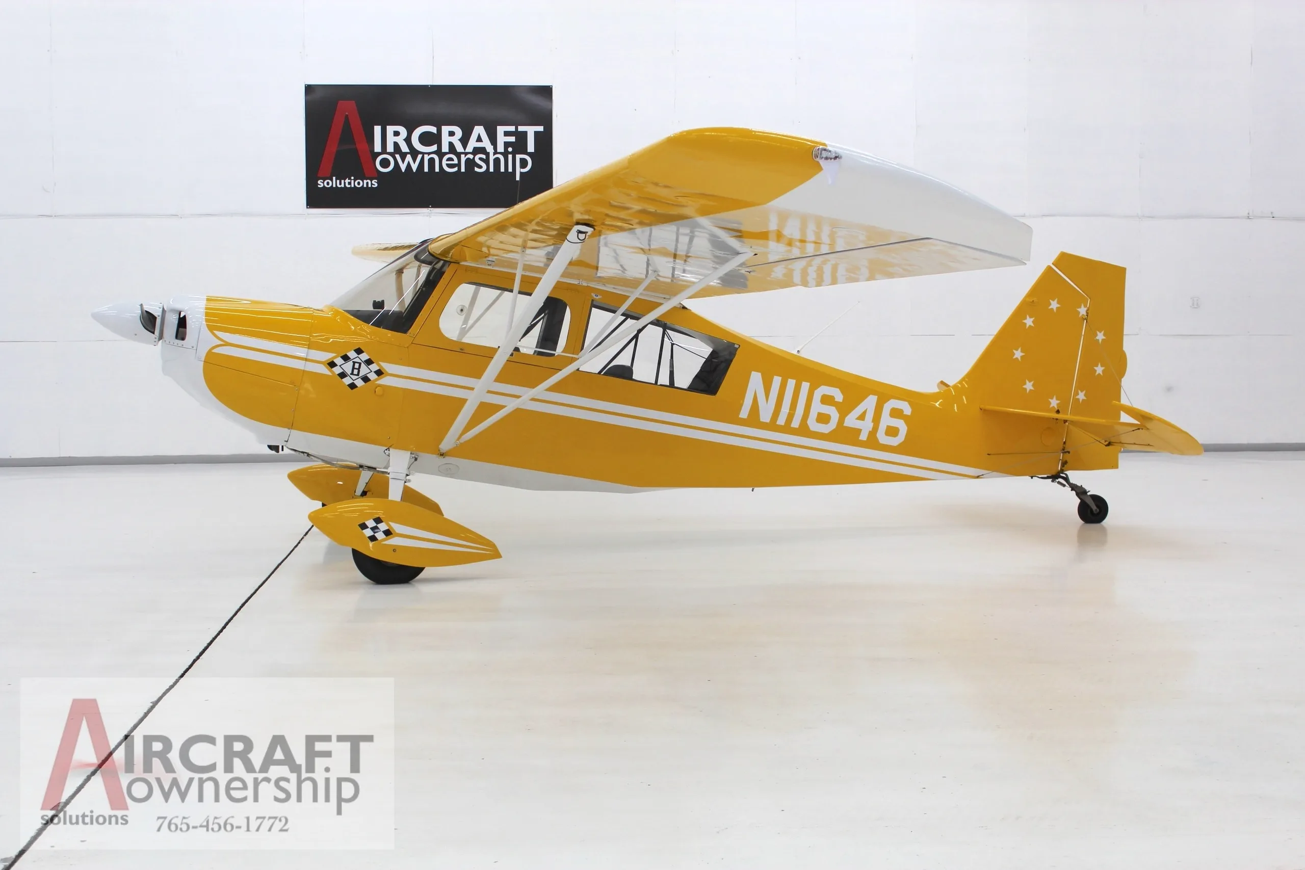 A yellow and white single-engine aircraft, N11646, with checkerboard accents and stars on the tail, is parked in a hangar.