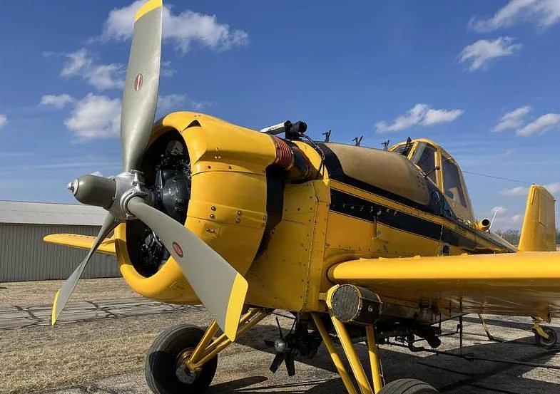 A close-up view of the front and side of a yellow agricultural aircraft, highlighting its propeller and engine cowling.