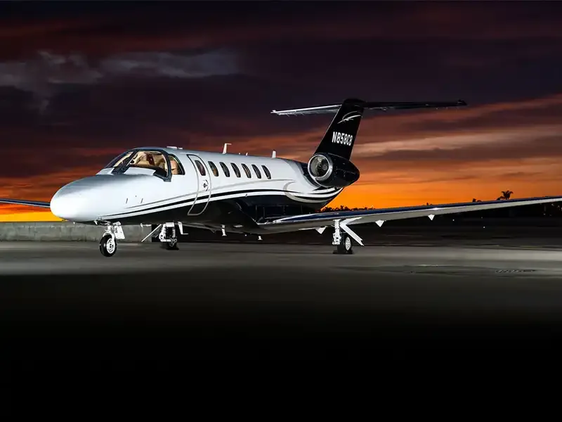 A silver and black private jet, likely a Cessna Citation, with registration N858C3, parked on a tarmac at sunset.