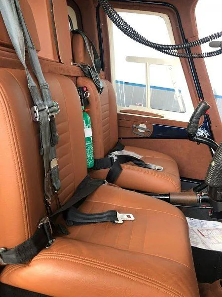 The brown leather interior seats of a helicopter are visible, with seatbelts and a fire extinguisher.
