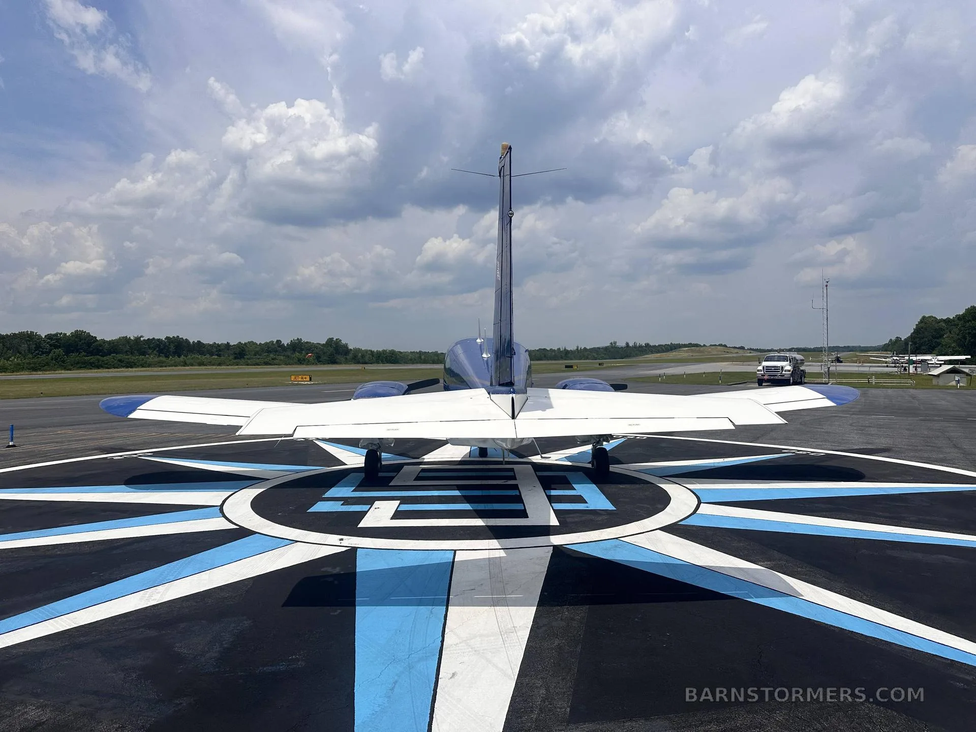 A rear view of a blue and white single-engine aircraft (N33SA) parked on a compass rose marking on an airfield.