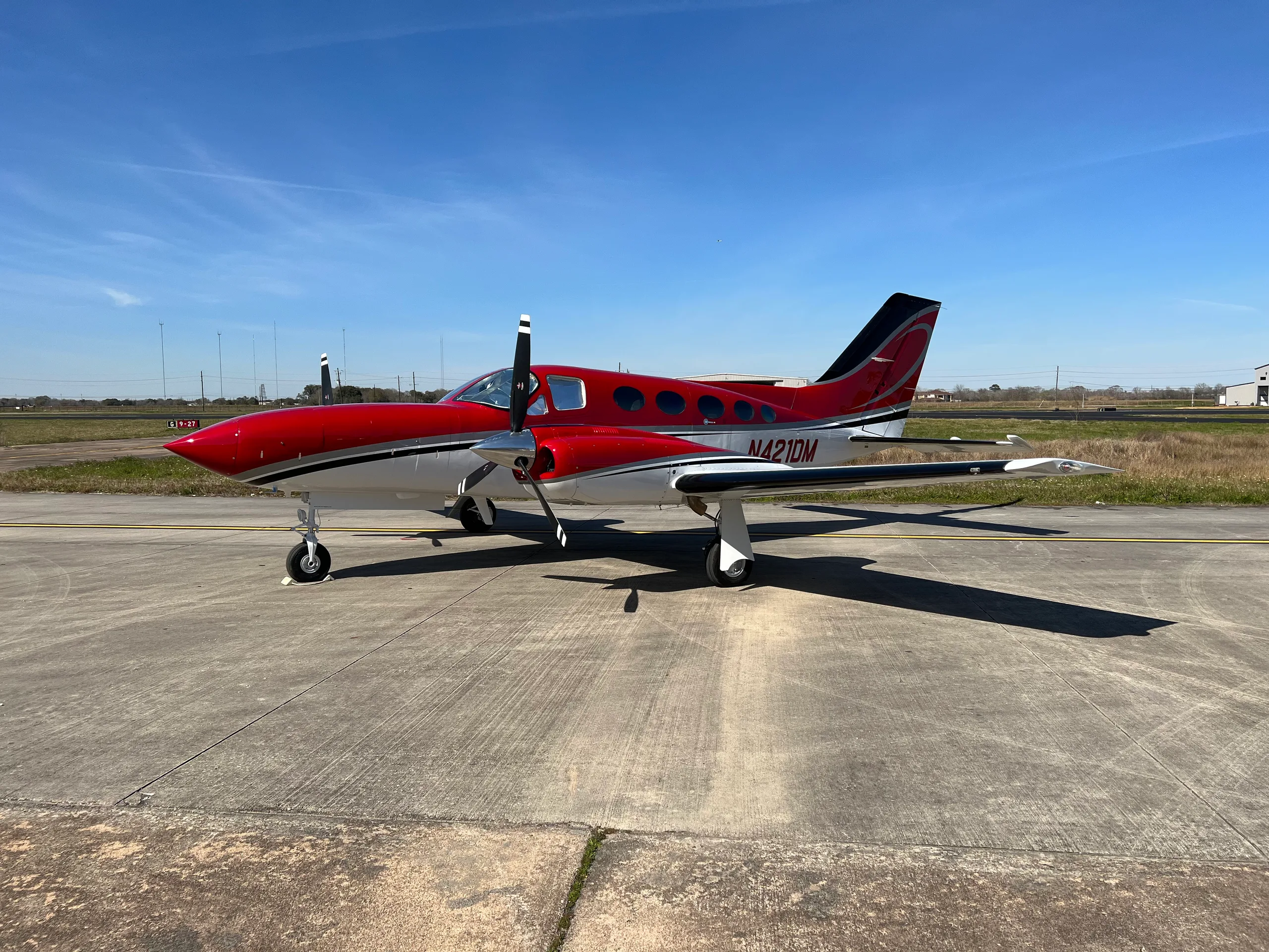 A red, white, and black twin-engine propeller aircraft, tail number N421DM, is parked on an airfield.