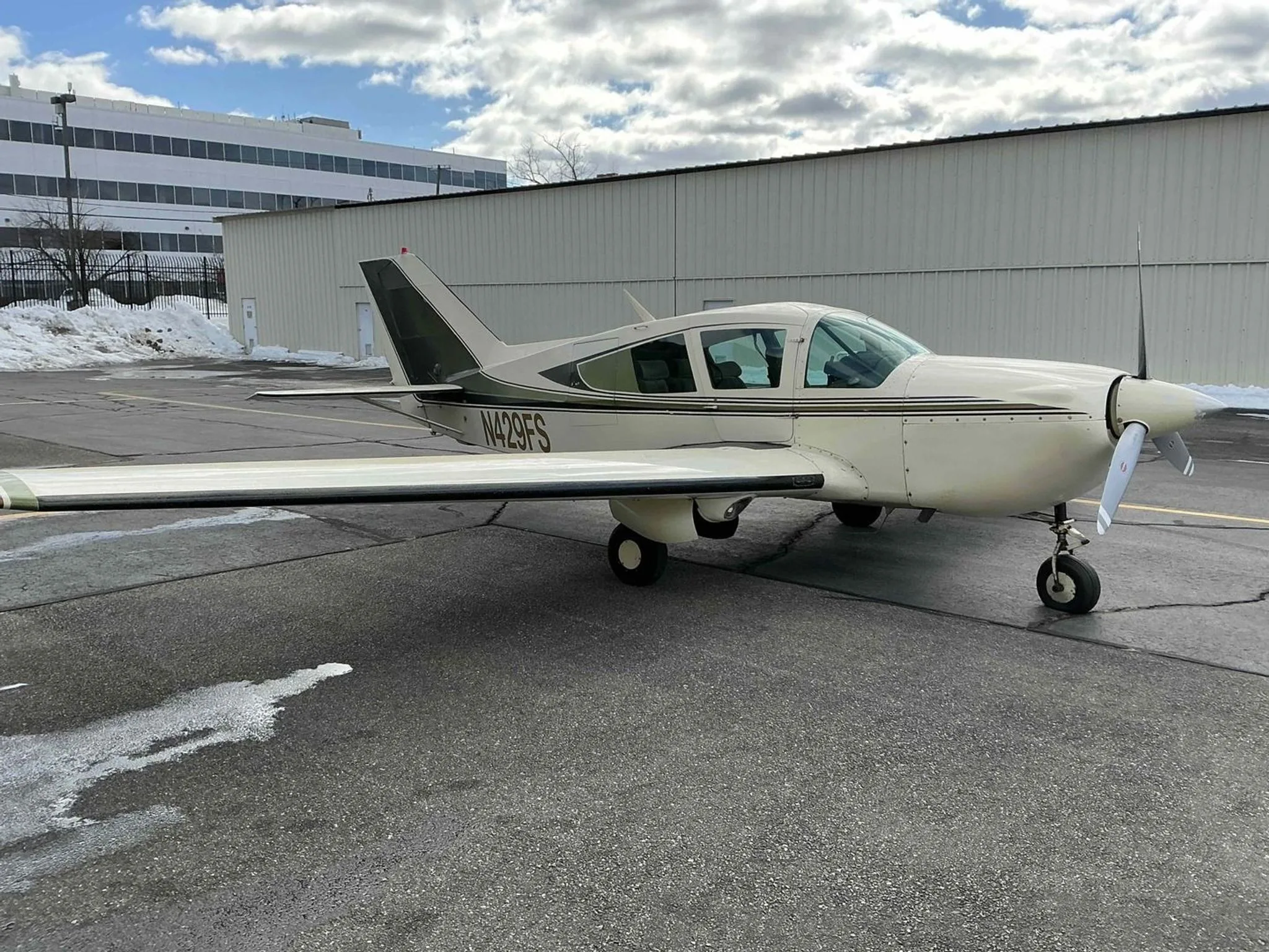 A white and green Bellanca Viking aircraft, N429FS, parked on an asphalt ramp with snow and a building in the background.