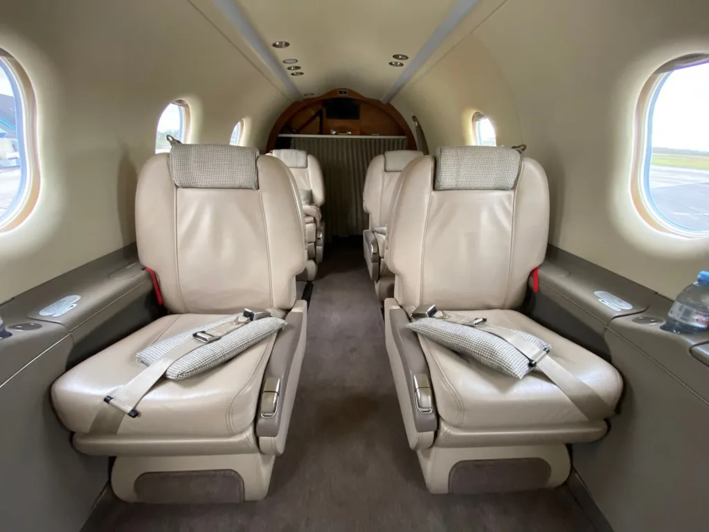 The beige leather interior cabin of an aircraft with four passenger seats visible, facing each other, from a slightly wider angle.