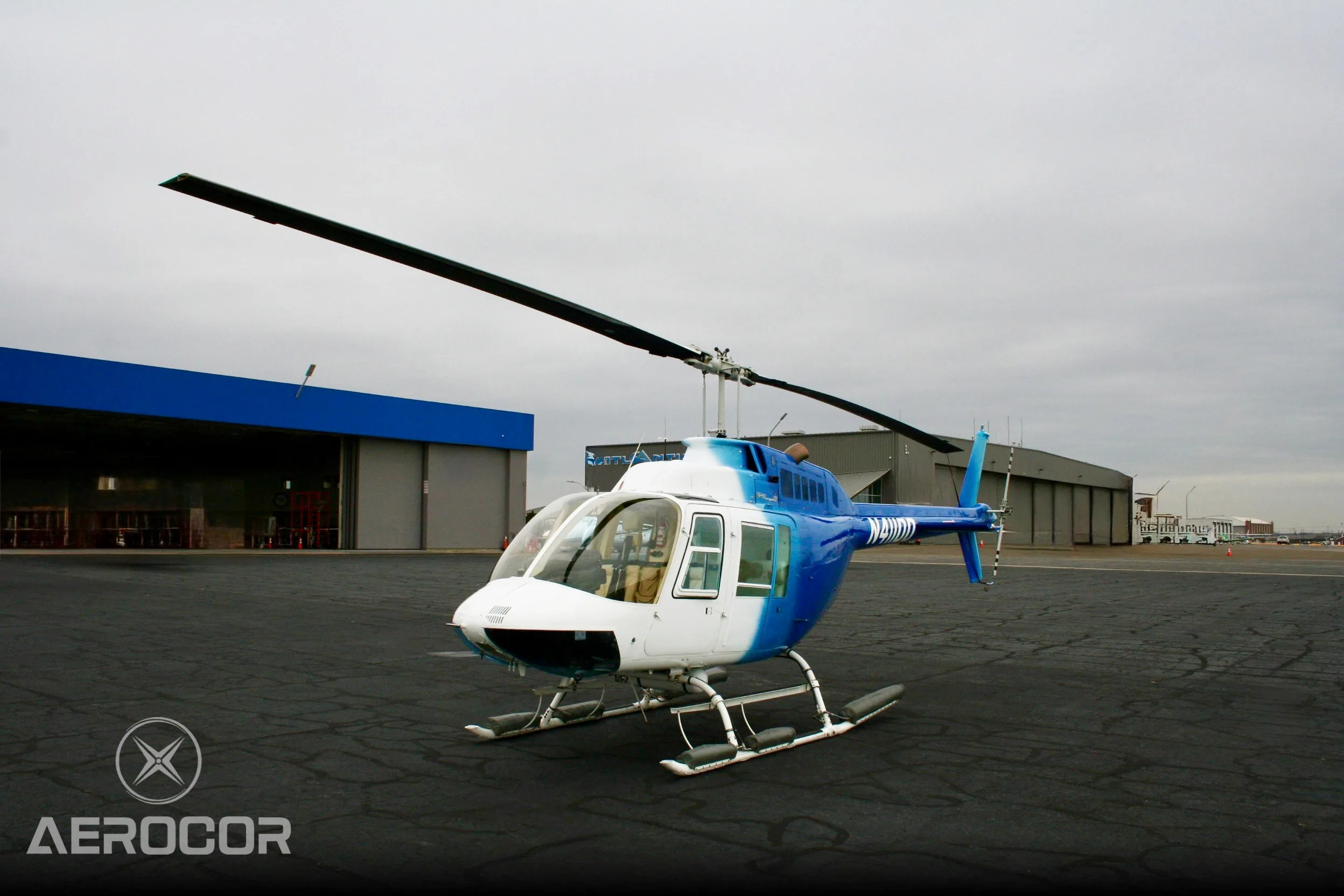 A front three-quarter view of a blue and white Bell JetRanger III helicopter, tail number N411DD, on an airport tarmac.