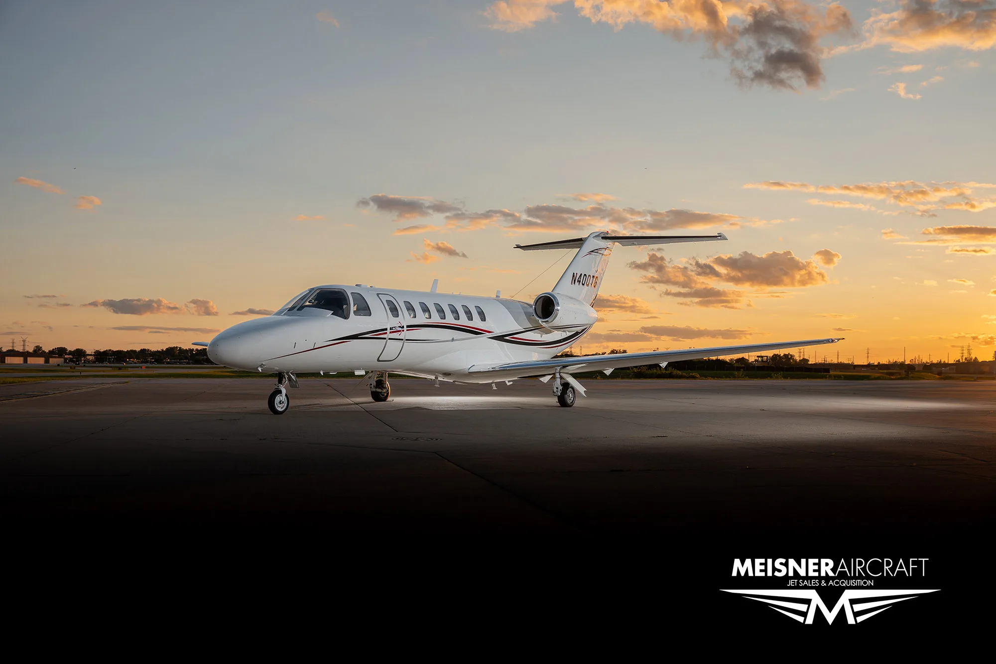 A white business jet with black and red stripes (N400TG) sits on a tarmac at sunset, with a 'Meisner Aircraft' logo.