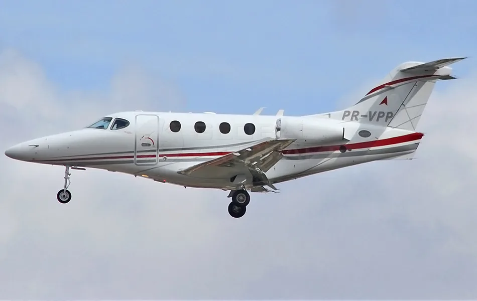 A white business jet with red and grey stripes, registration PR-VPP, flying with landing gear extended against a cloudy sky.