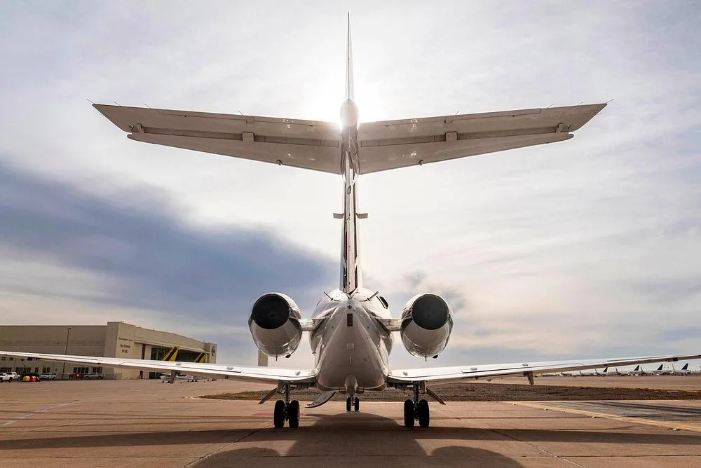 A rear view of the business jet on a tarmac, with the sun glinting over its tail.