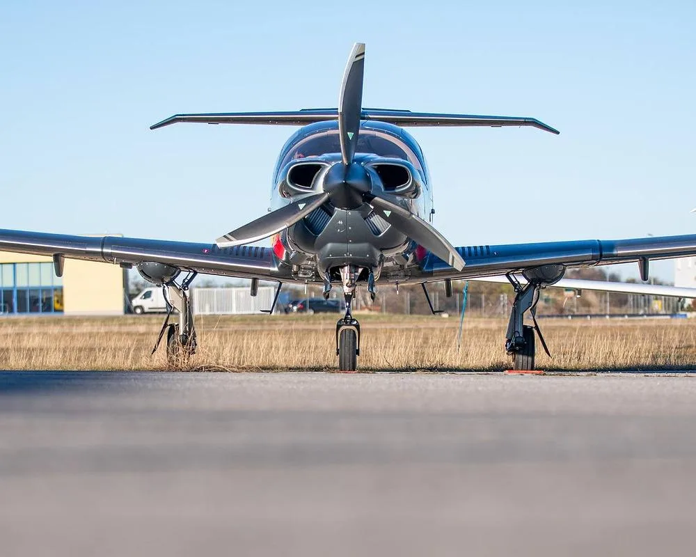 A dark grey and red Diamond DA62 aircraft is parked on an airfield, viewed from the front.