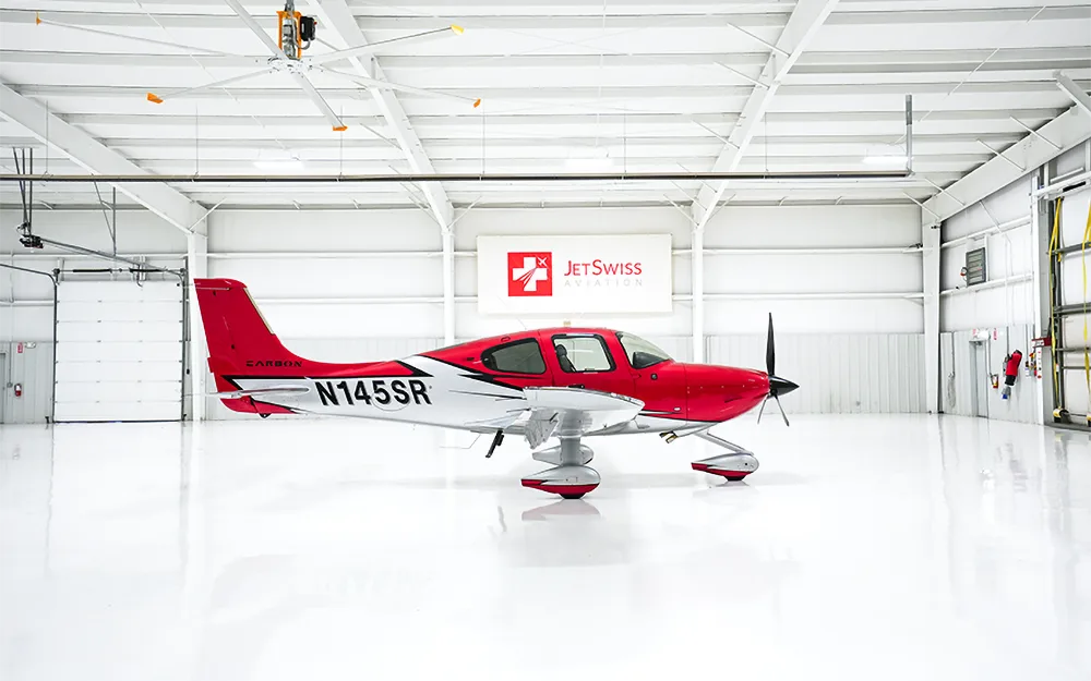 A red and white Cirrus SR22 aircraft with registration N145SR parked inside a clean white hangar.