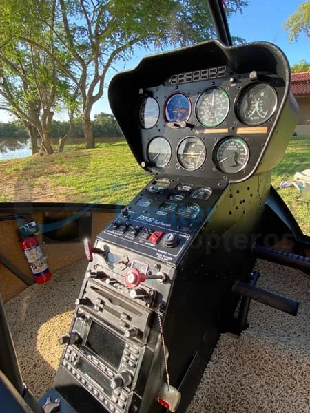 The cockpit of a Robinson R66 Turbine helicopter shows the instrument panel, controls, and a fire extinguisher.