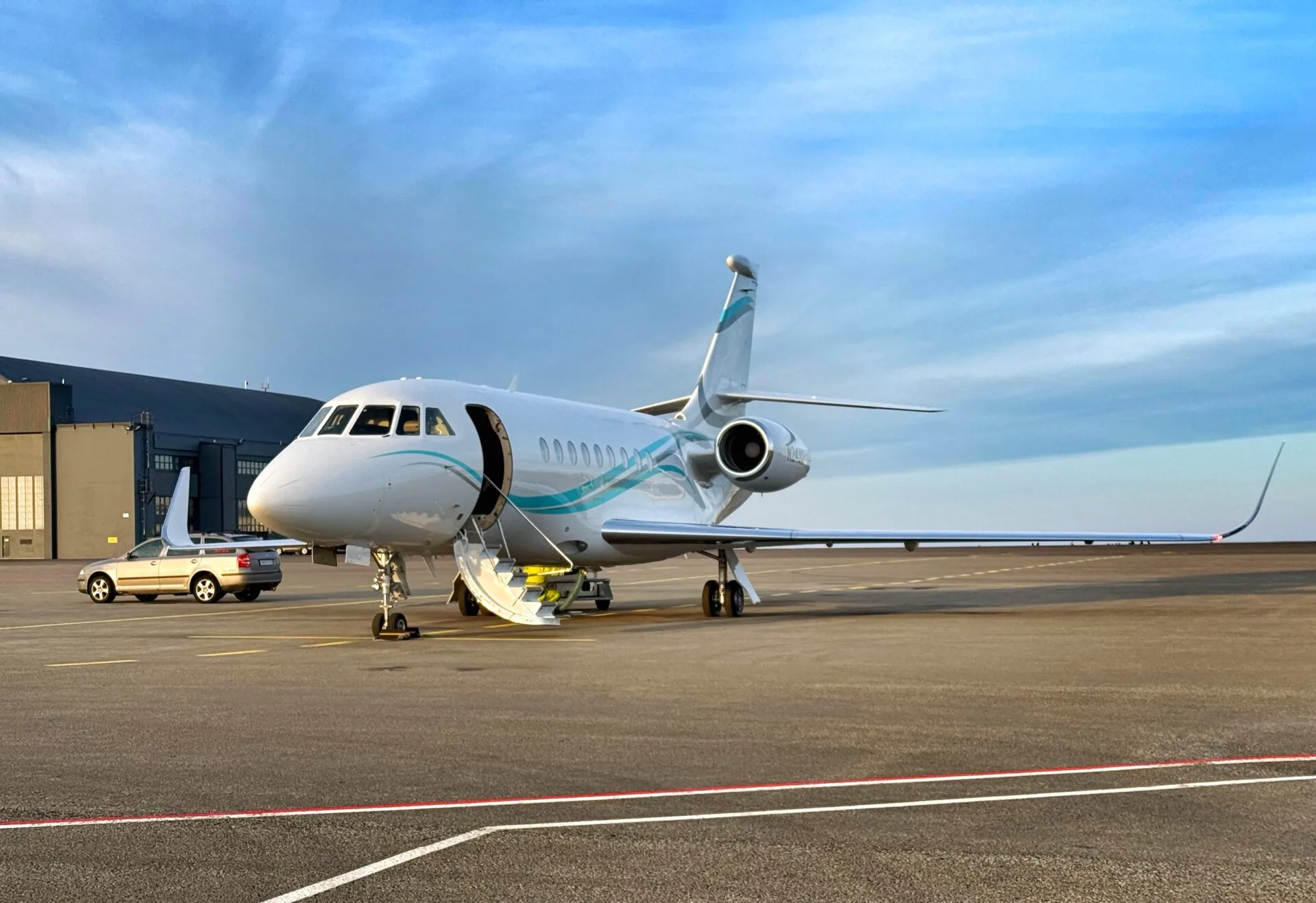 A white business jet with blue and teal stripes on the fuselage and tail, parked on an airfield with its door open.
