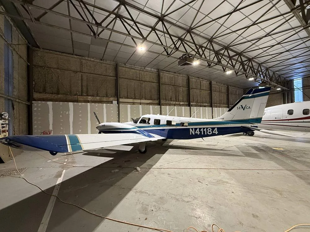 Side view of a Piper Seneca aircraft with registration N41184, featuring a white and blue paint scheme, parked in a hangar.
