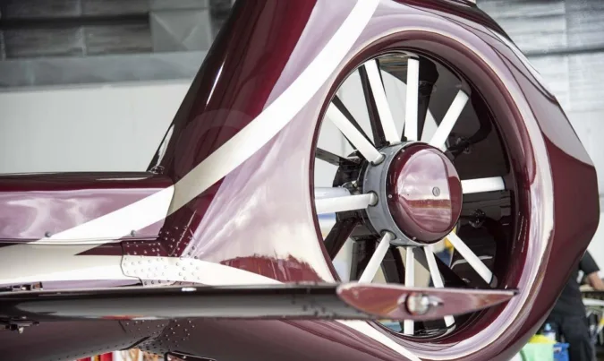 A close-up view of the fenestron tail rotor of a burgundy helicopter with white stripes.