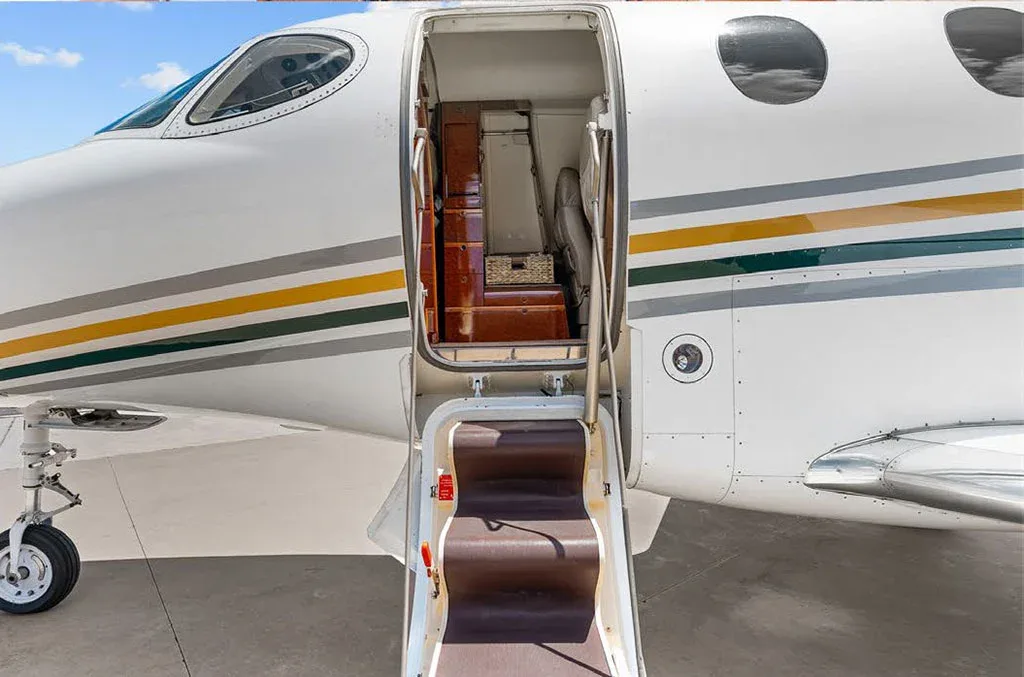 The open entry door and integrated steps of a white private jet, revealing a glimpse of the interior.