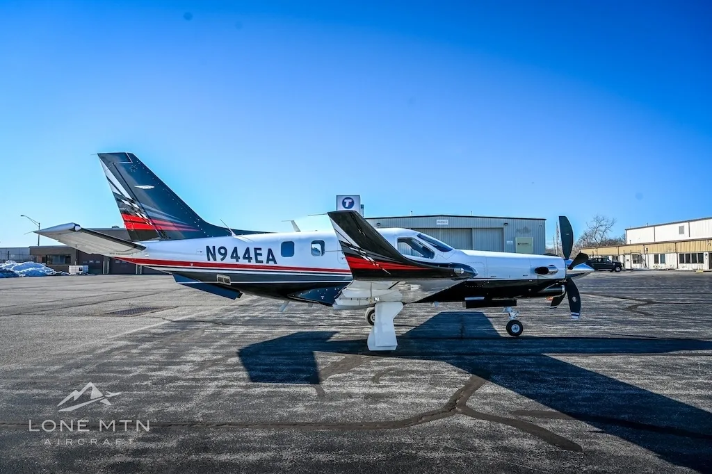 A TBM 940 aircraft, registration N944EA, parked on an asphalt ramp with a hangar in the background.