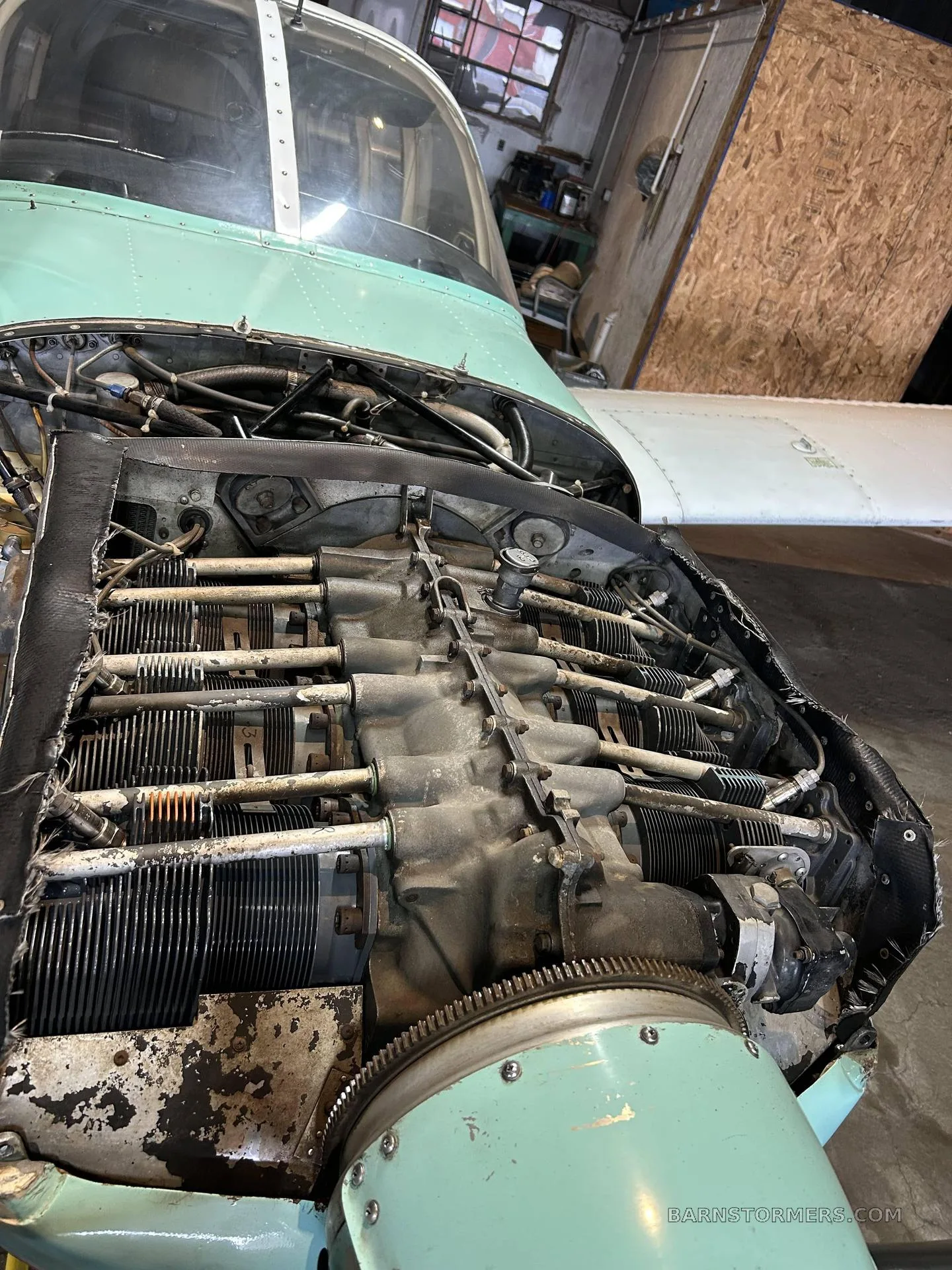 A close-up view of the exposed engine of a light green and white aircraft, showing cylinders and components.