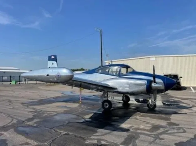 A silver and blue twin-engine aircraft, N708T, parked on a tarmac with hangars in the background.