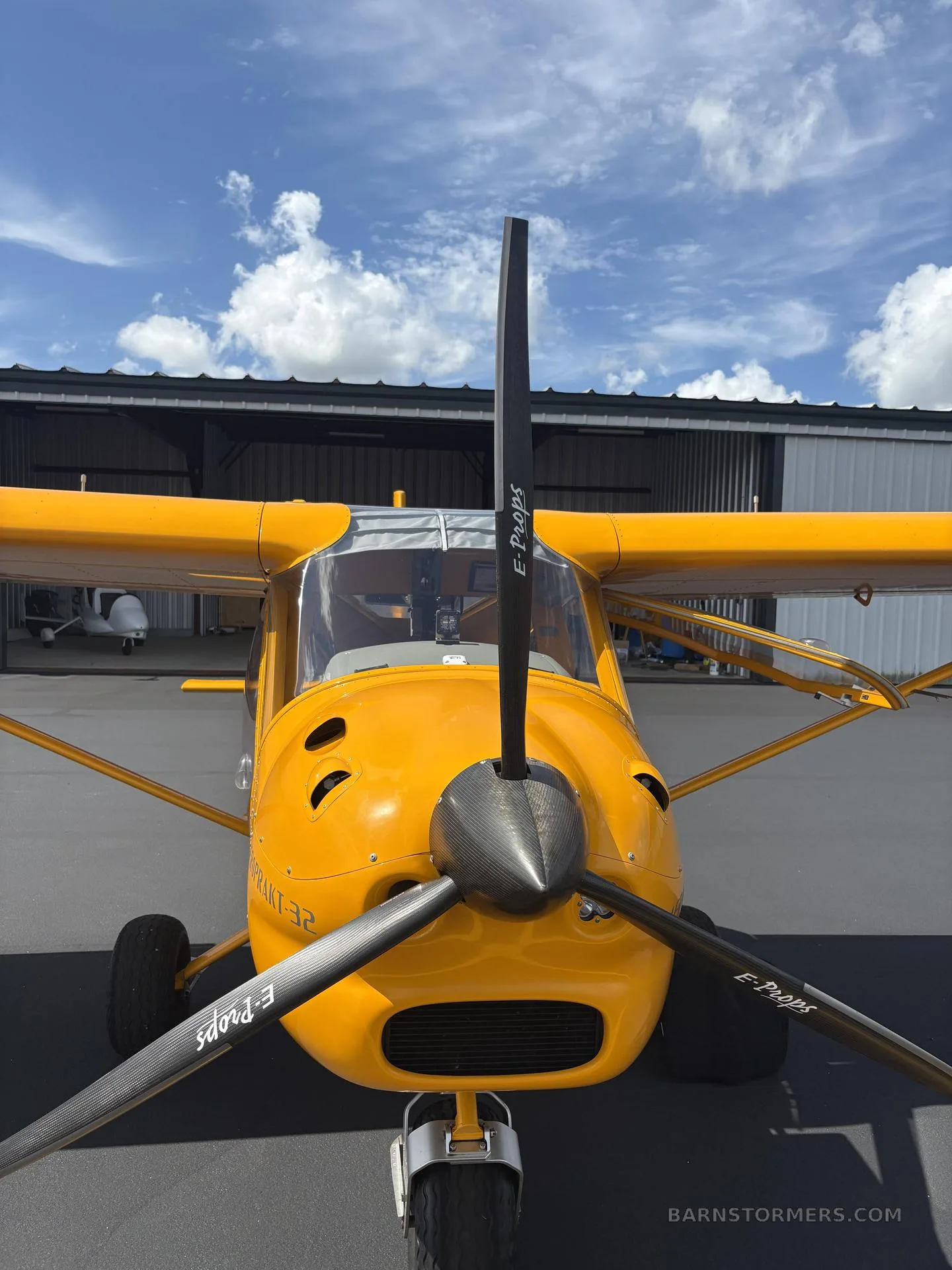 A head-on view of the yellow Aeroprakt A-32 Light Sport aircraft, showing its propeller and front landing gear.