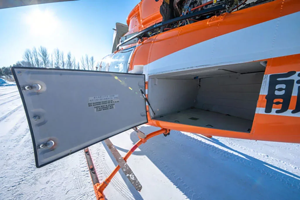 A close-up view of the open cargo compartment on the side of the orange and white Bell 407 helicopter.