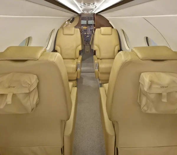 Interior view of the aircraft cabin with tan leather seats and life vest pouches.