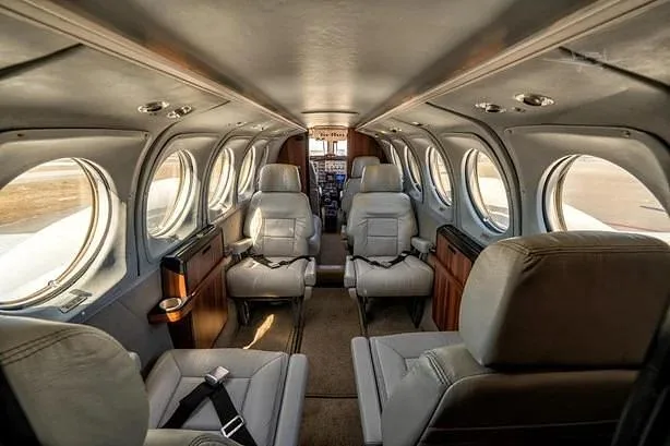 The interior cabin of a private aircraft features light gray leather seats and large oval windows.