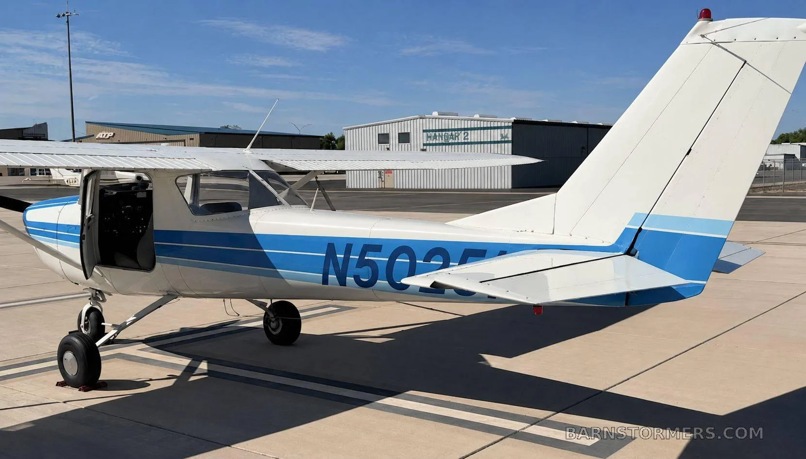 A side-rear view of a white and blue single-engine propeller aircraft, showing the tail number N50251, parked on an airfield.