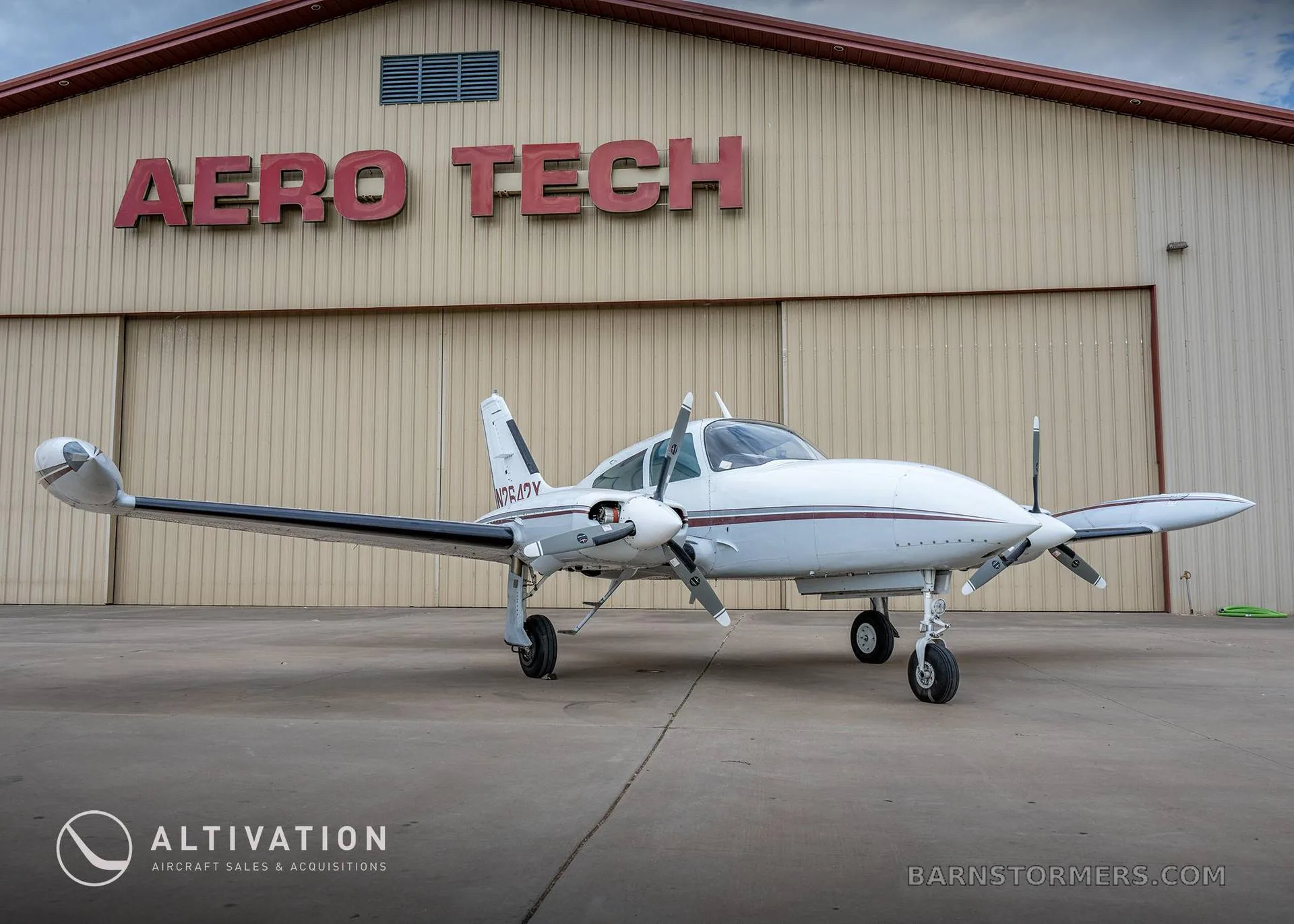 A white twin-engine propeller aircraft with maroon stripes, registration N2642Y, parked in front of a hangar with "AERO TECH" written in red.