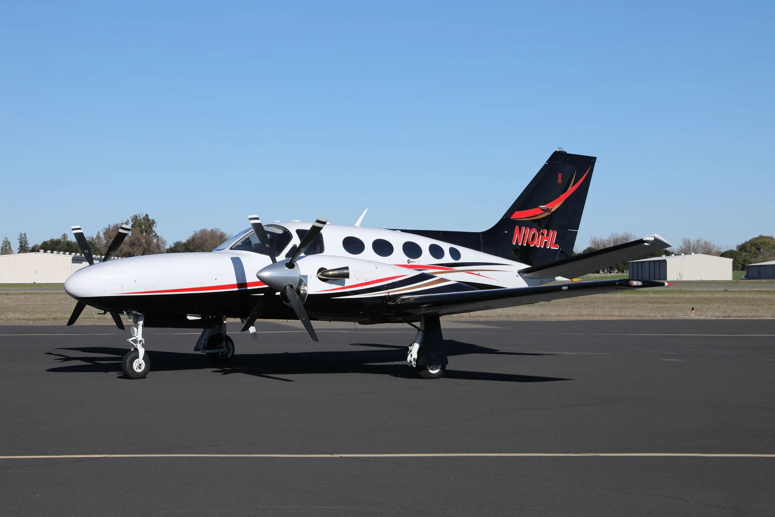 A white, black, and red Cessna 414 Chancellor parked on an asphalt tarmac under a clear sky.