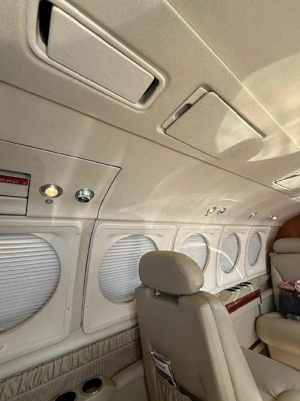 A view inside the aircraft cabin showing beige ceiling panels, overhead lights, and windows with closed blinds.