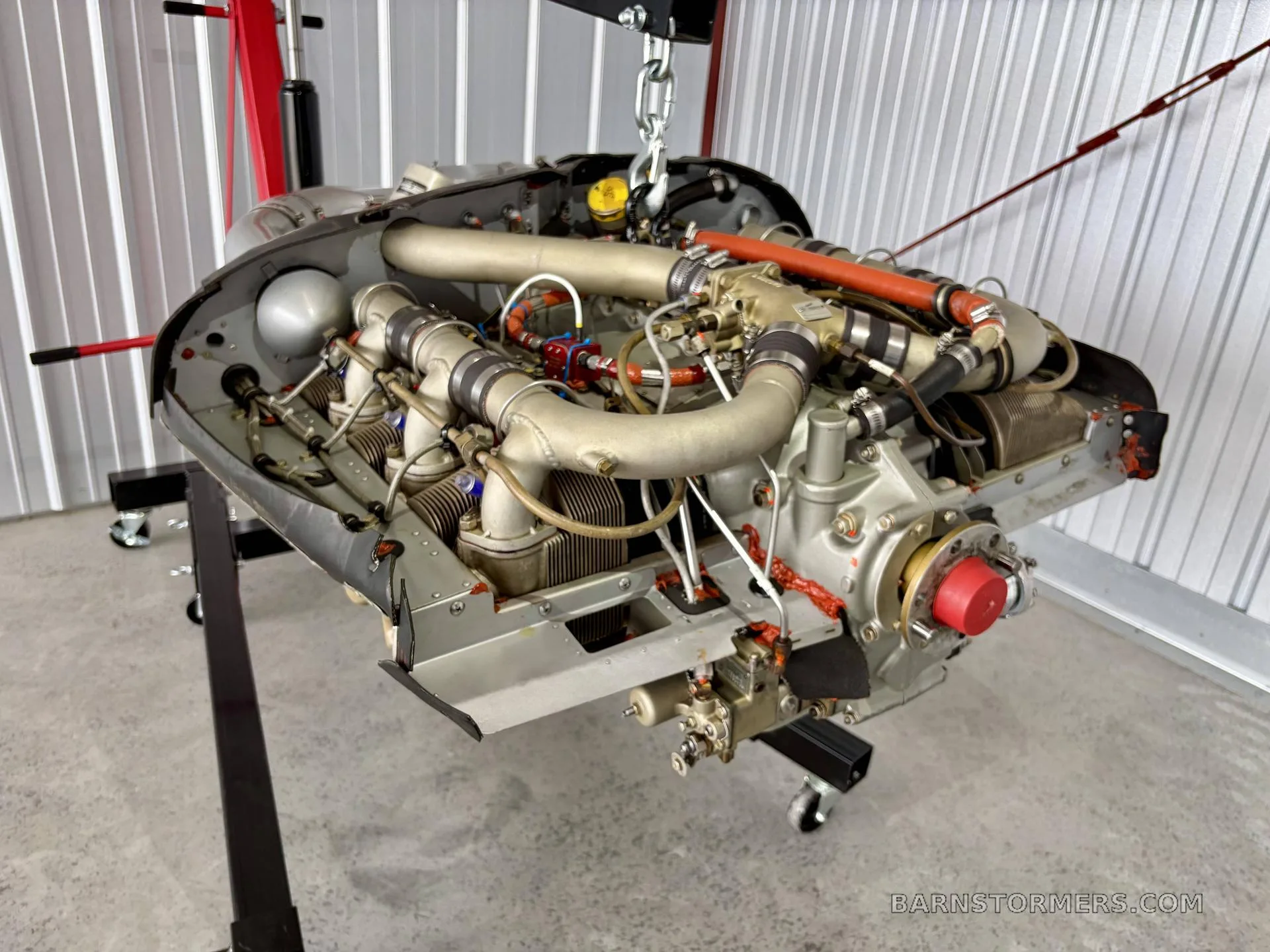 A Teledyne Continental aircraft engine, suspended by a hoist, in a hangar.