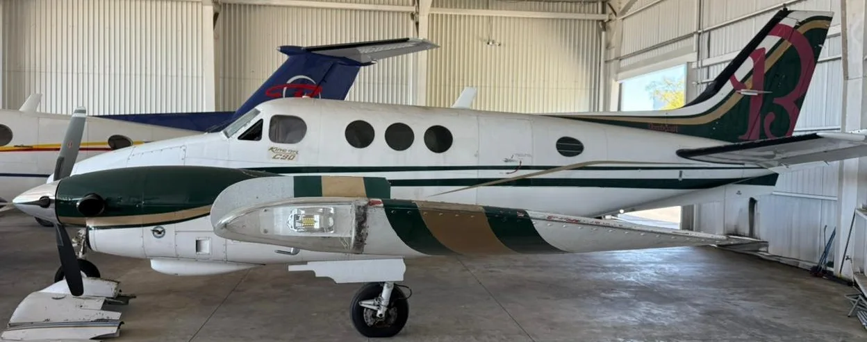 Side view of a white and green King Air C90 turboprop aircraft in a hangar.