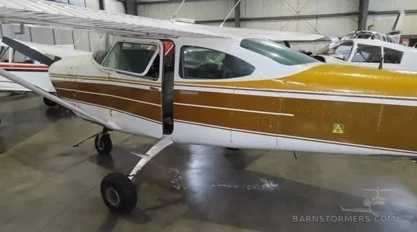 A white and gold Cessna 172 with its door open, parked in a hangar, viewed from the side.