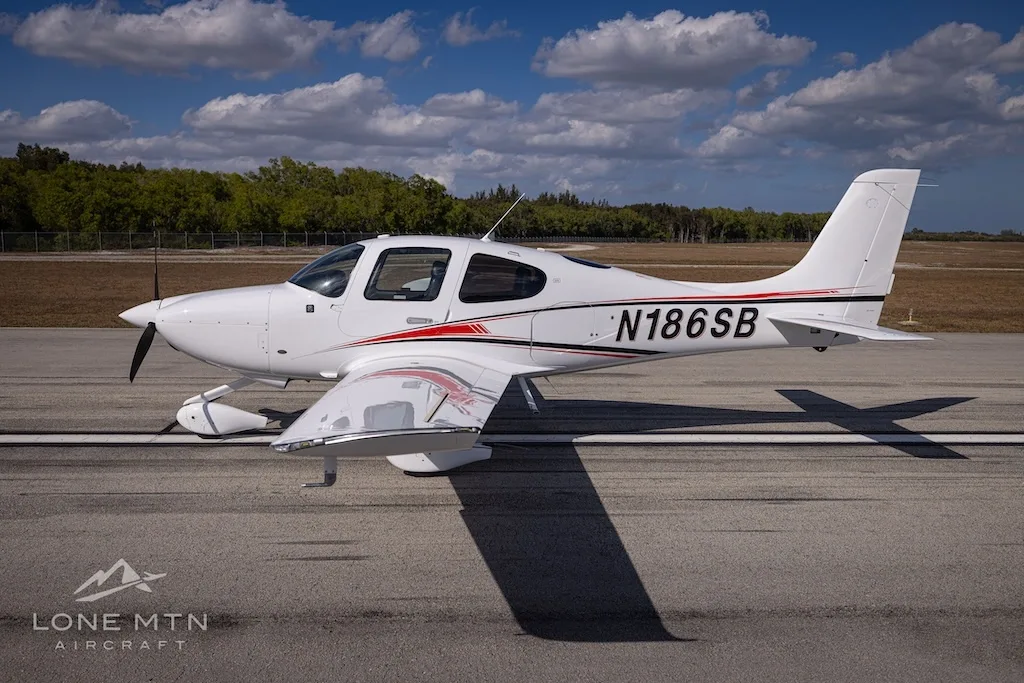 A side view of the white N186SB single-engine aircraft with red and black stripes, parked on an airfield.
