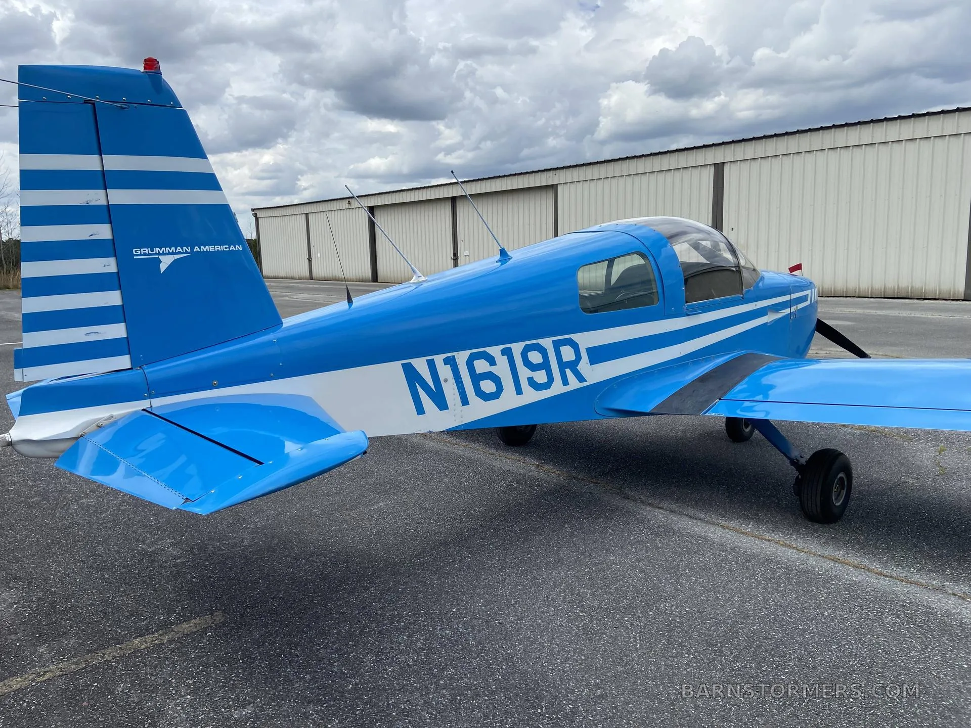 A blue Grumman American aircraft (N1619R) with white stripes parked on the tarmac, viewed from the rear-left.