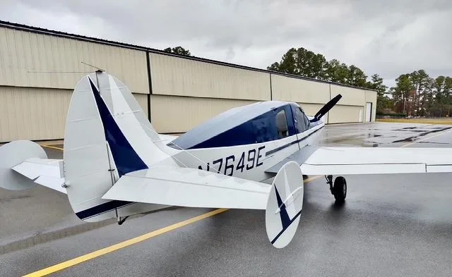 A rear view of the white and blue Bellanca 7GCBC Citabria N7649E parked on a wet tarmac.