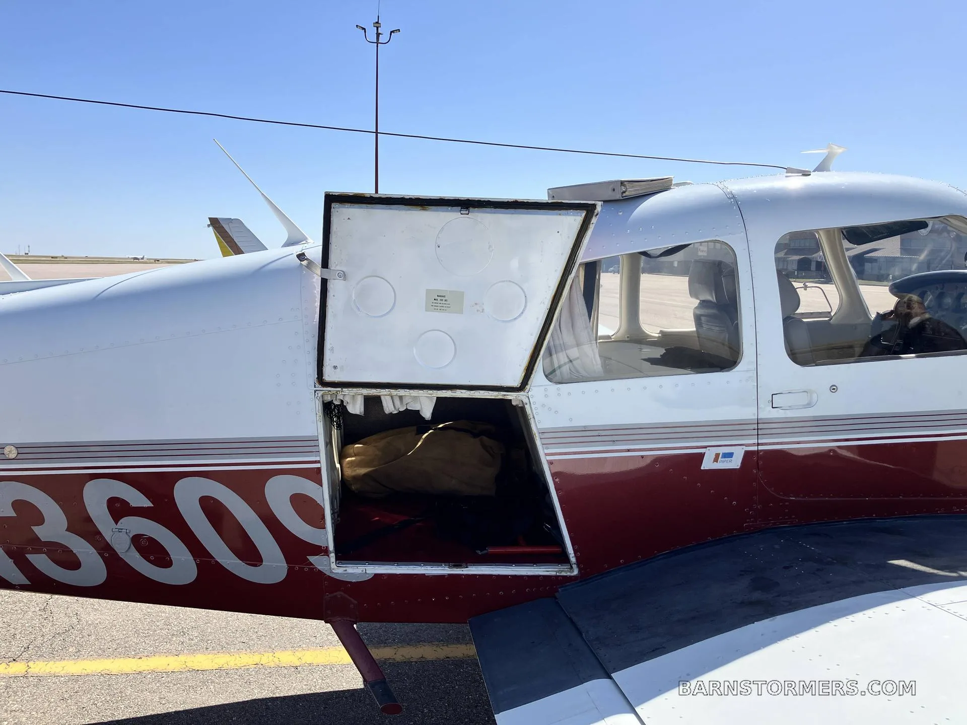 A close-up of the white and maroon aircraft's fuselage with the baggage compartment door open, revealing a bag inside.