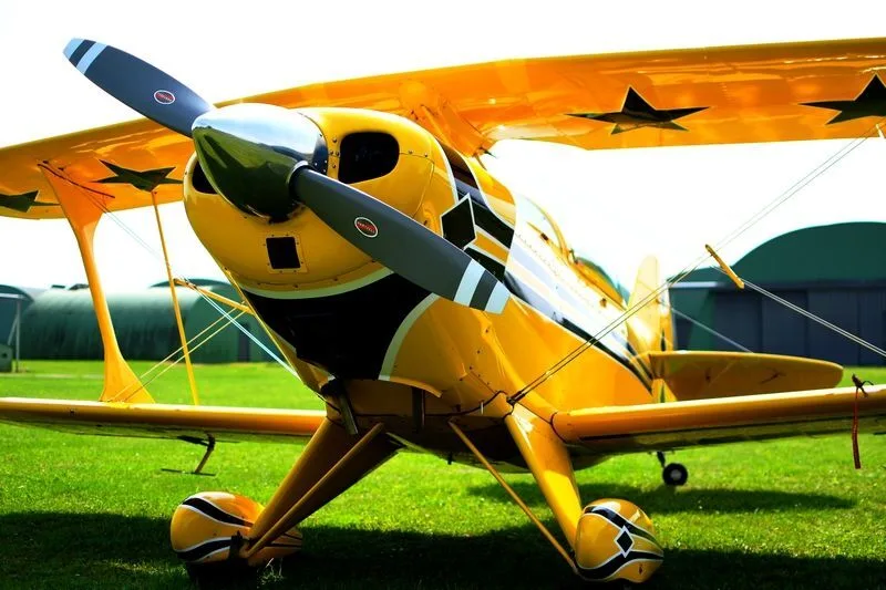 A yellow biplane with black and white accents and stars on the wing, seen from the front-right on a grassy field.