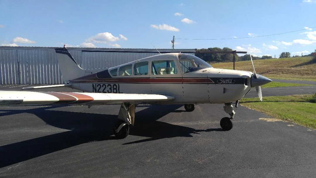 A white and brown single-engine aircraft, N2238L, parked on an airfield next to a hangar.