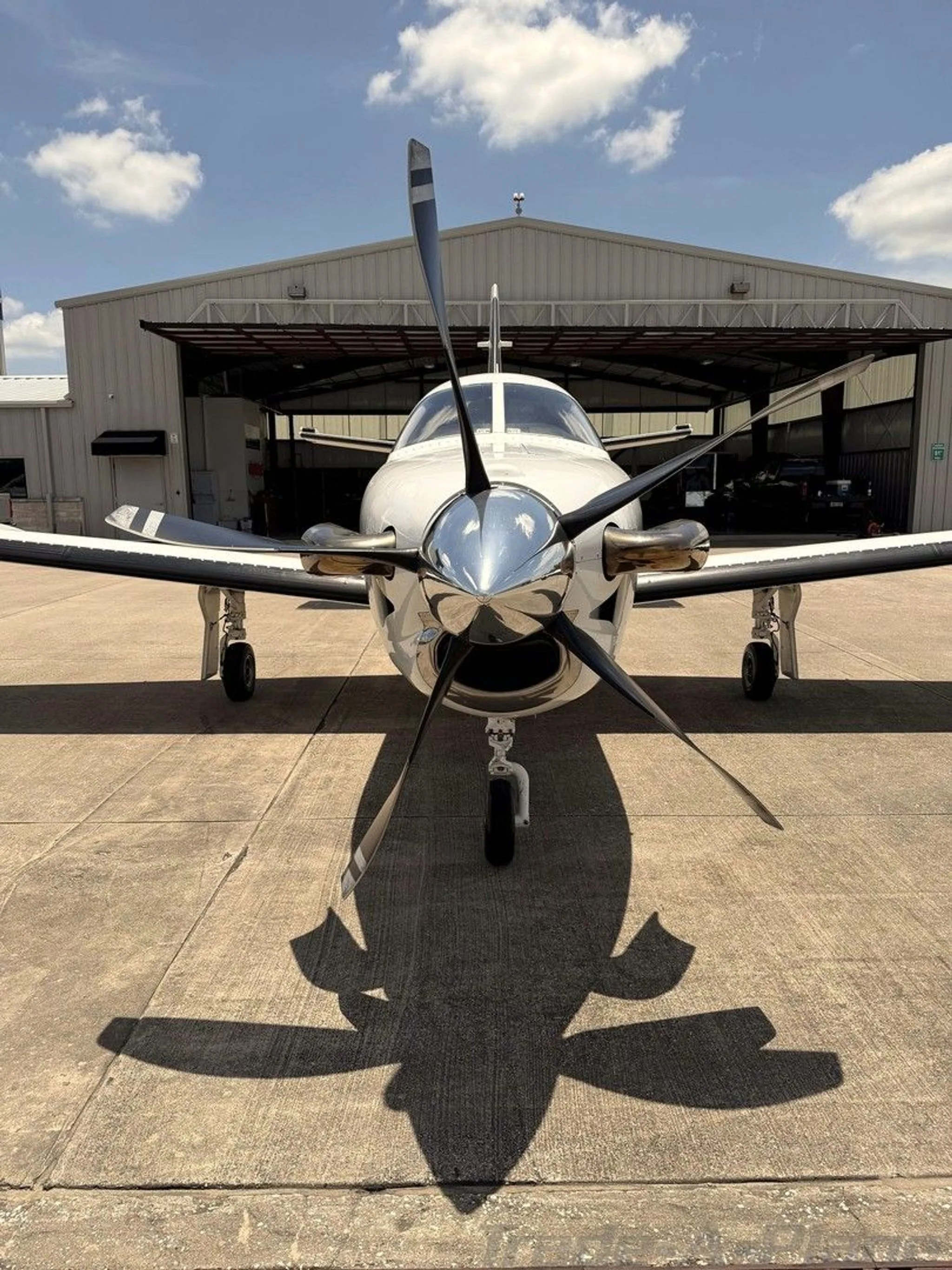 Front view of a white turboprop aircraft with black stripes parked in front of a hangar.