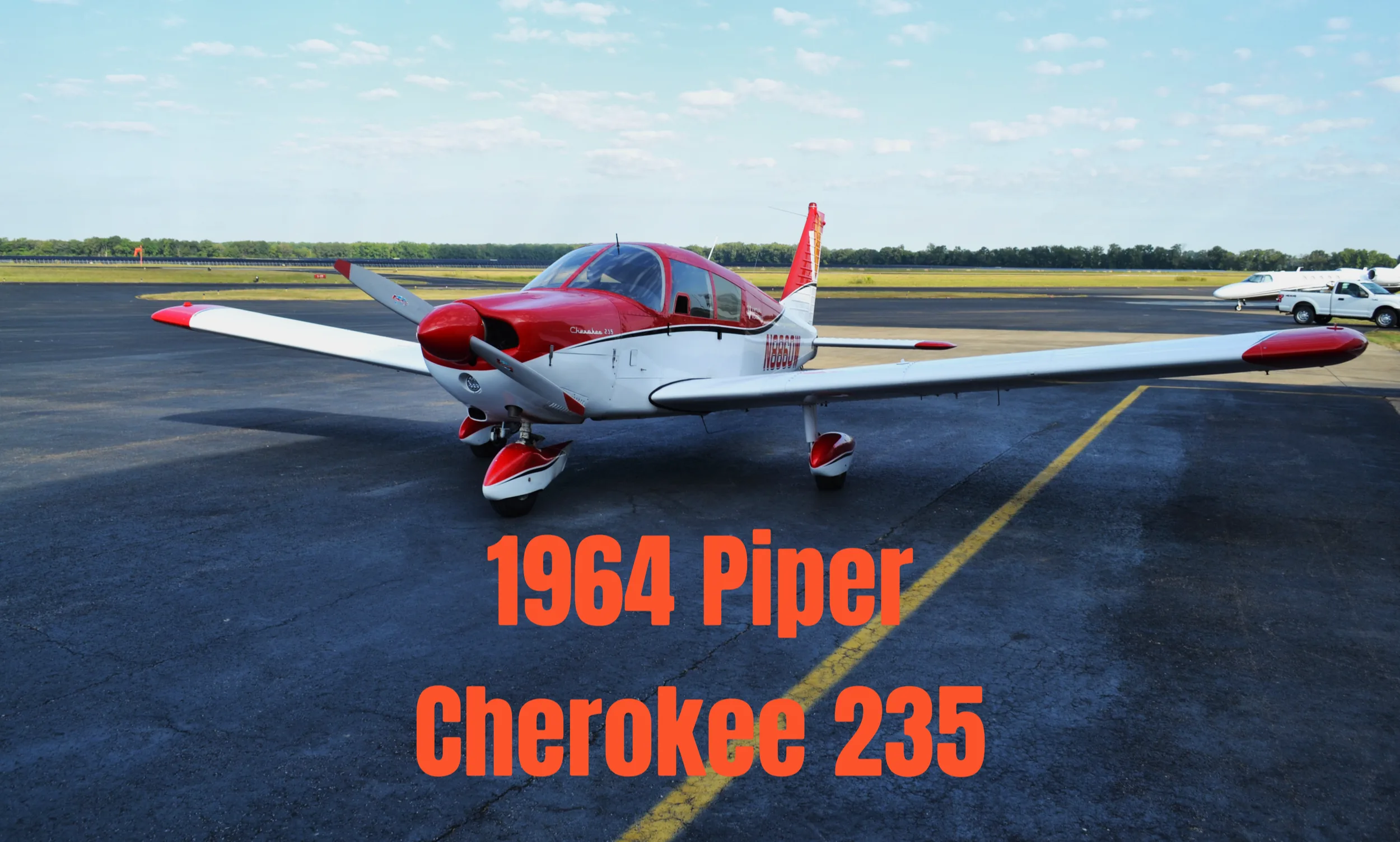 A red and white 1964 Piper Cherokee 235 aircraft is parked on an airport tarmac under a blue sky.