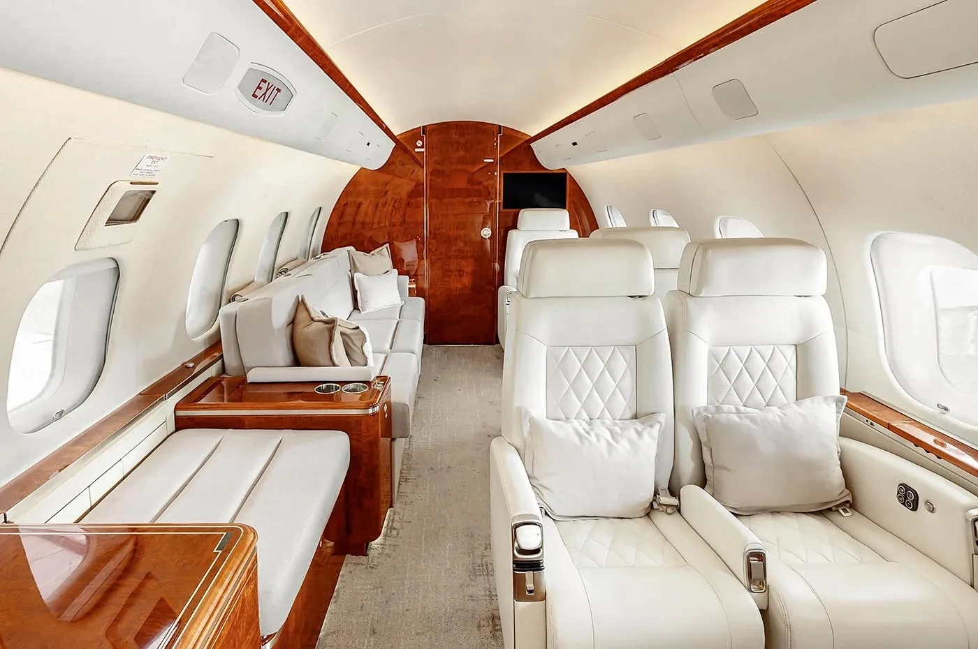 The luxurious cabin of a business jet features light-colored quilted leather seats, a lounge area, and polished wood accents.