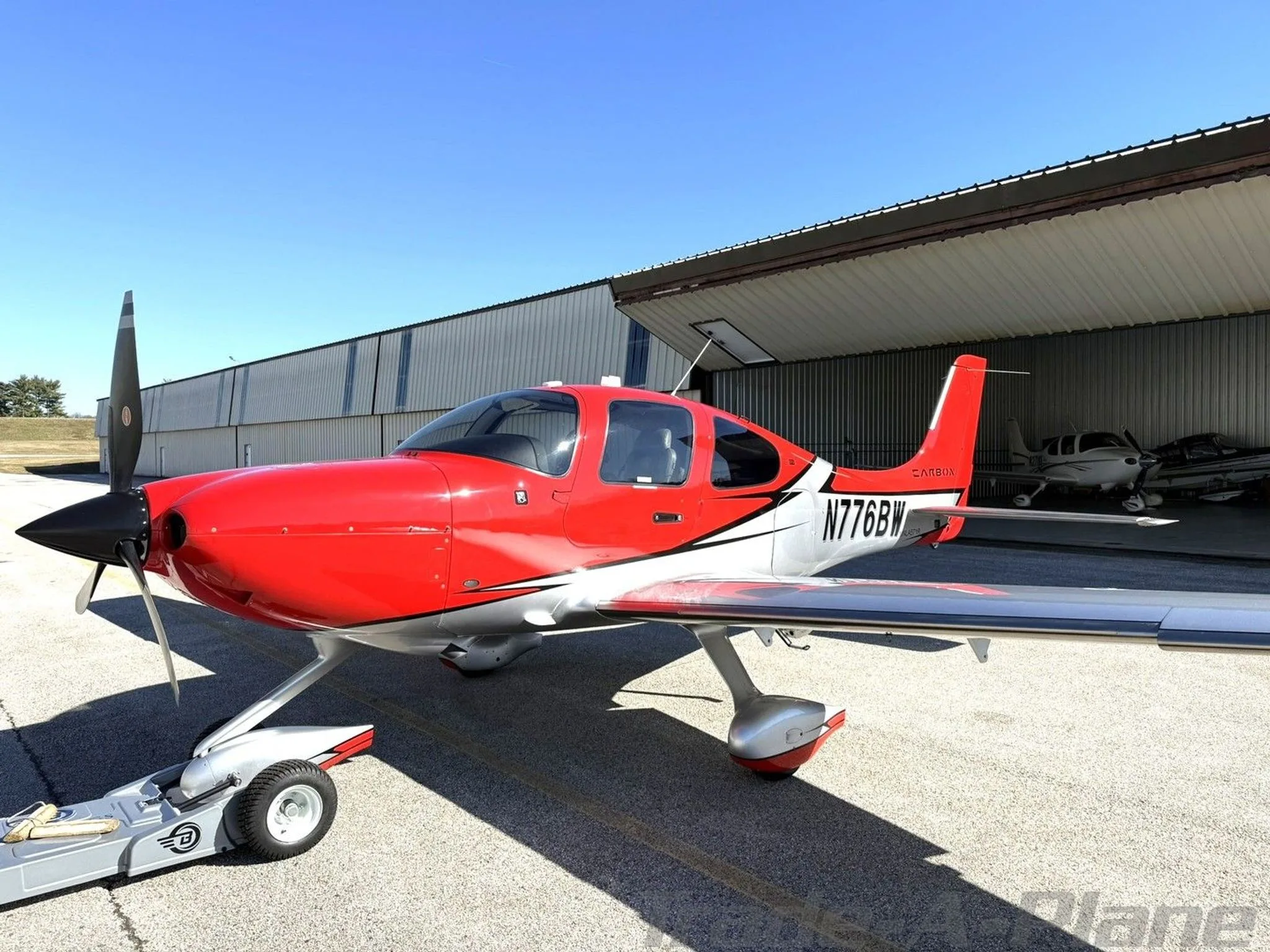A red and silver Cirrus SR22T aircraft, N776BW, parked on the tarmac in front of a hangar.