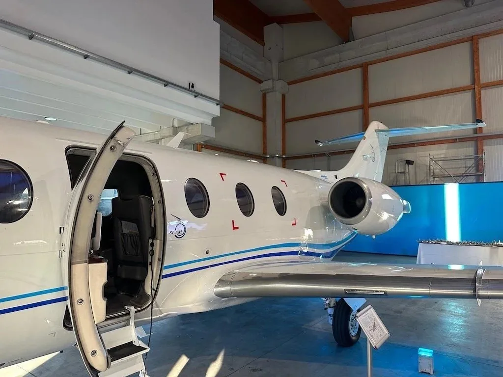 A white business jet with blue stripes has its main cabin door open, revealing the steps and interior, parked in a hangar.