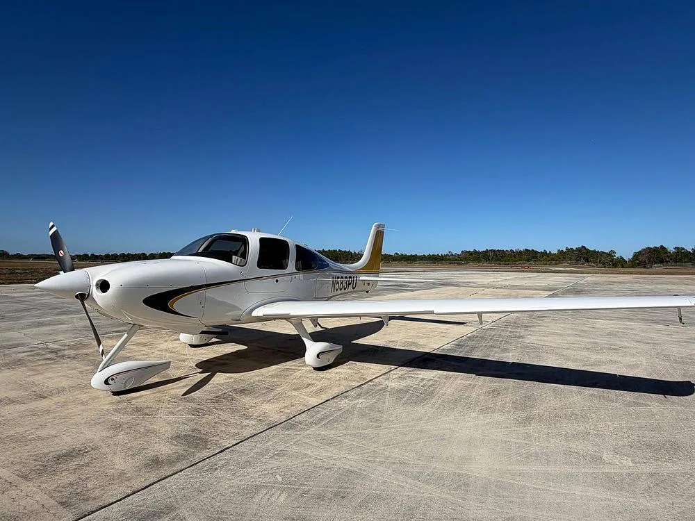 A side view of a white Cirrus SR22 aircraft with black and gold stripes and a gold tail, registration N583PU, on an airfield.