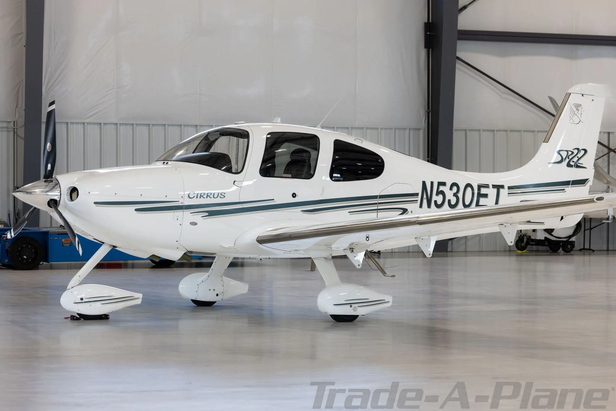 A white Cirrus SR22 aircraft with N530ET registration and green stripes is parked in a hangar, viewed from the front left.