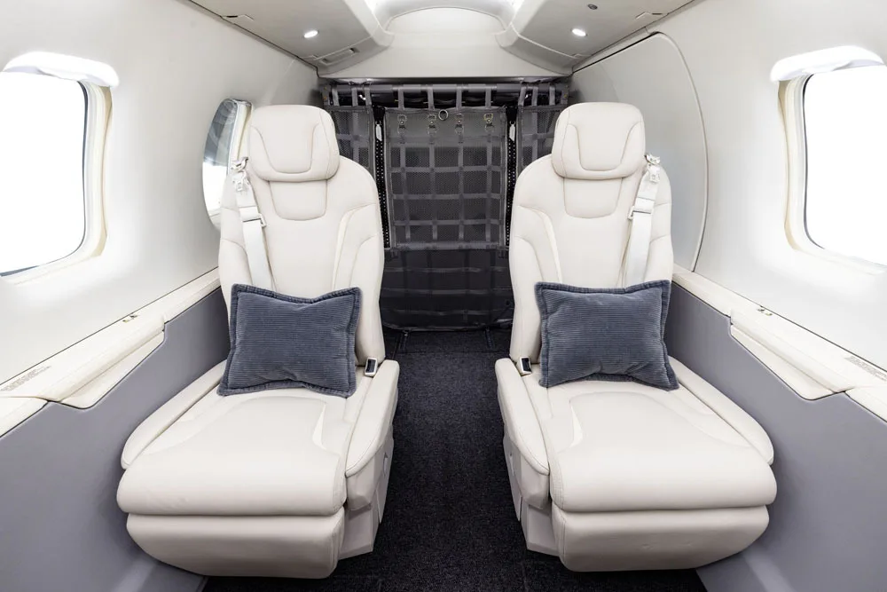 The rear section of a private jet cabin with two light beige seats facing forward and a cargo net behind them.