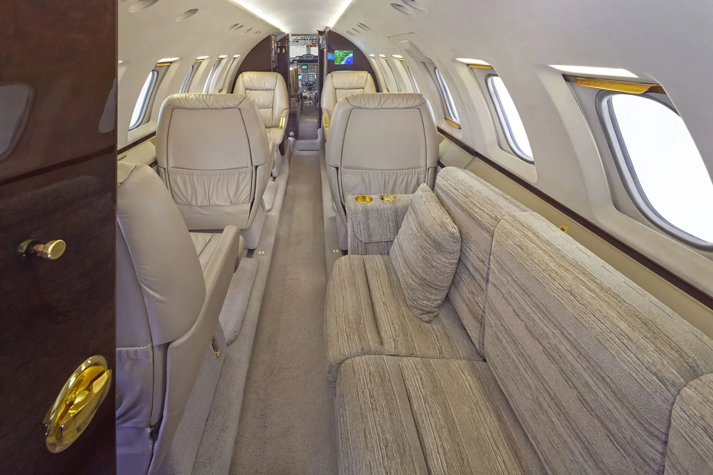 The interior of a private jet cabin, showing a long beige sofa on the right and individual cream leather seats on the left.