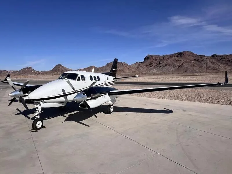 A white and black twin-engine turboprop aircraft parked on an airfield with mountains in the background.