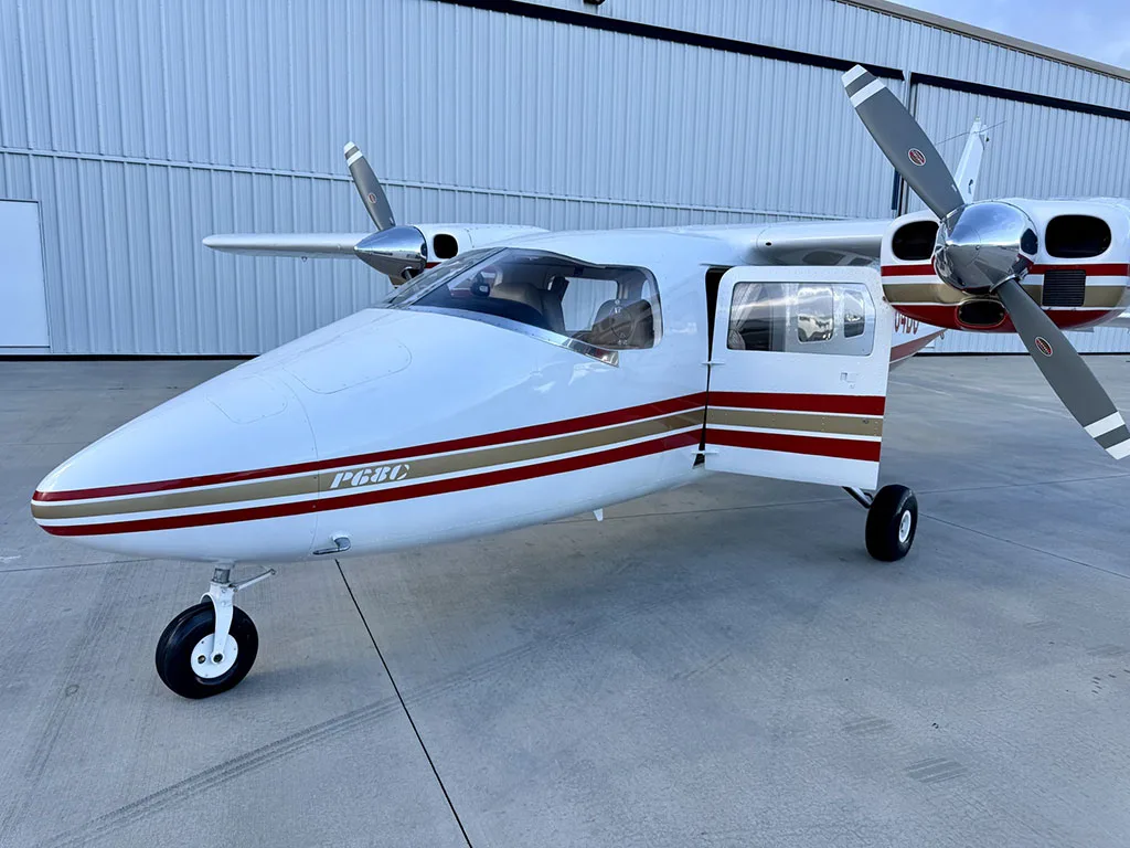 A front-side view of the white and red twin-engine aircraft, N564BC, with its passenger door open on an airport tarmac.